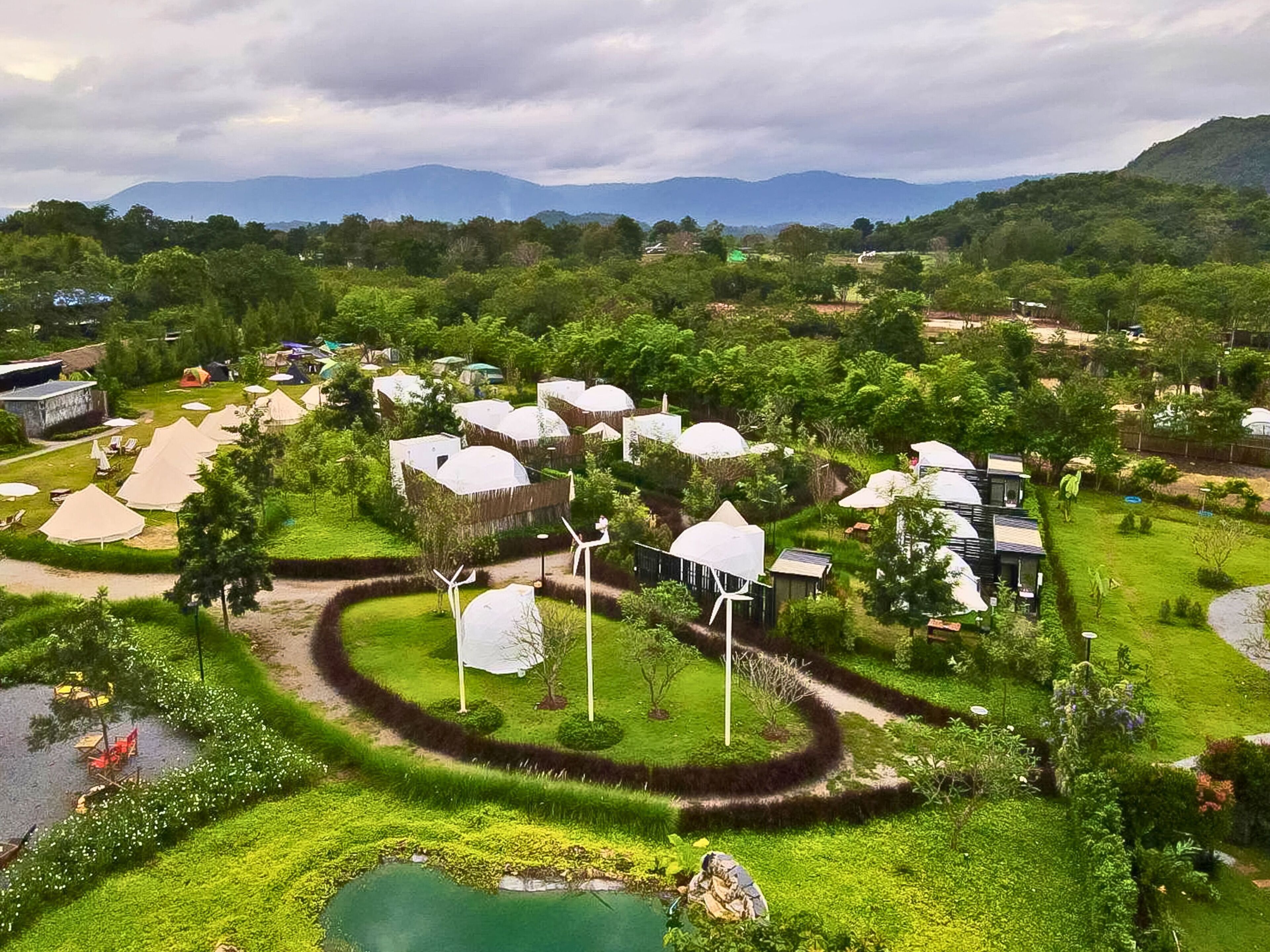 A resort with thatched-roof huts, a central pond, and wind turbines.