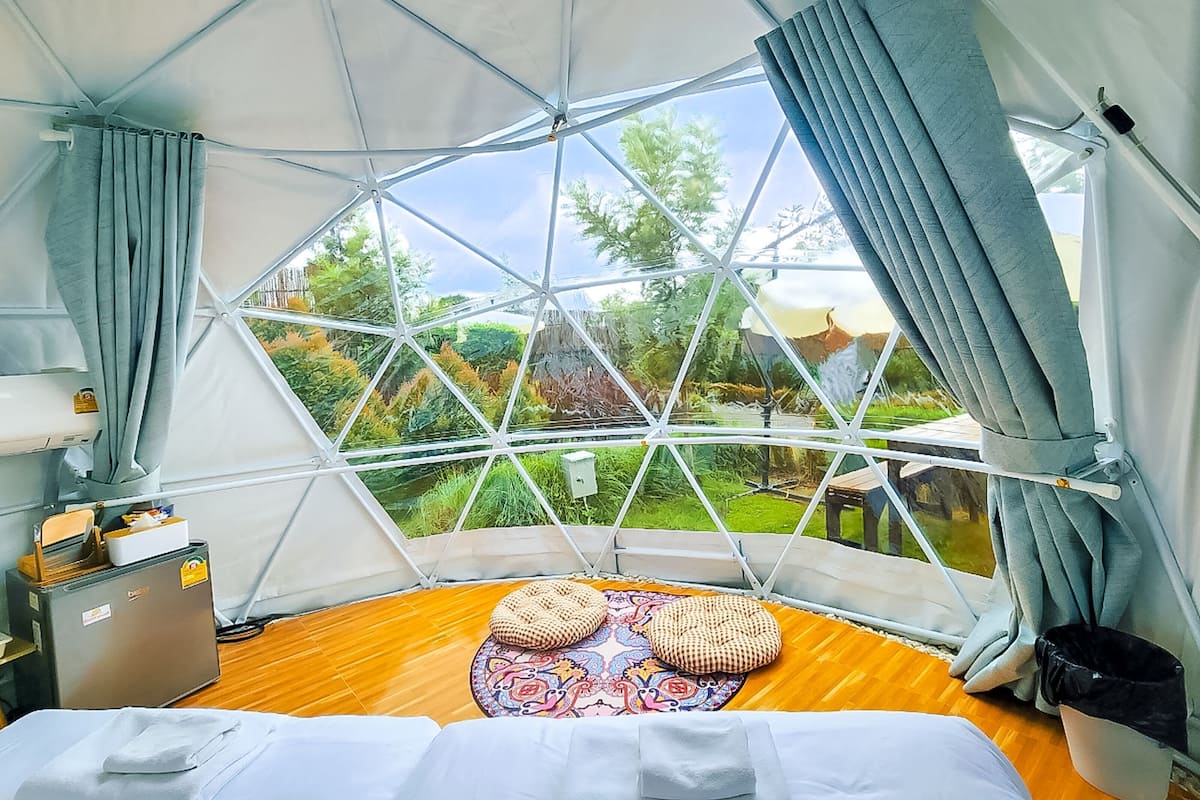 Ein geodätisches Kuppelzelt mit einem Bett, einem kleinen Tisch und Blick auf einen Garten.