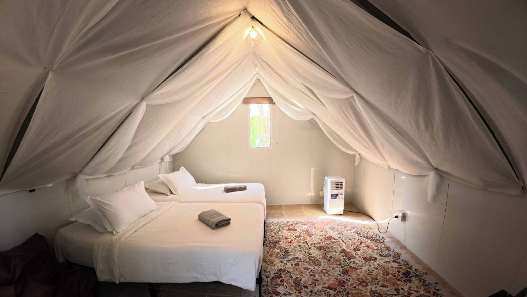 A cozy tent-style room with two beds, a small window, and a heater.