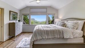 Un dormitorio con cama, cómoda, ventilador de techo y ventanas amplias que ofrecen vistas al exterior.