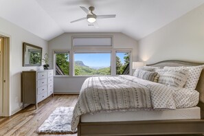 Una camera da letto con un letto, una cassettiera, una ventola a soffitto e ampie finestre che offrono vista sull'esterno.