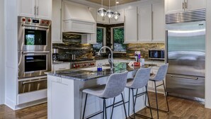A modern kitchen with a central island, stainless steel appliances, and a stone backsplash. - The View From Up Here Changes Everything | Big Bear Pen (Highlands)