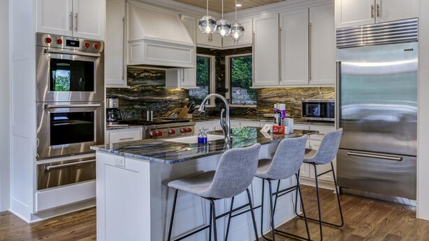 Una cocina moderna con una isla central, electrodomésticos de acero inoxidable y un protector contra salpicaduras de piedra.