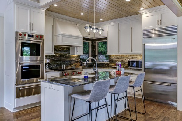 A modern kitchen with a central island, stainless steel appliances, and a stone backsplash. - The View From Up Here Changes Everything | Big Bear Pen (Highlands)