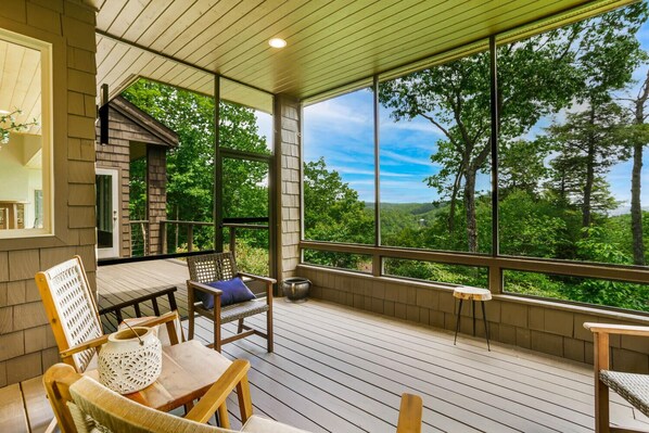 A covered outdoor deck with wooden furniture, large windows, and a view of a forested landscape. - The View From Up Here Changes Everything | Big Bear Pen (Highlands)