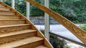 Una escalera de madera con un muro de piedra y ventanas de vidrio que dan a un área boscosa.