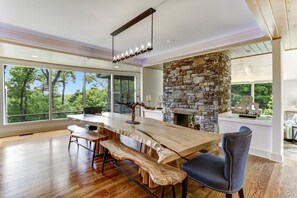 A spacious dining area with a large wooden table, stone fireplace, and a view of the outdoors.