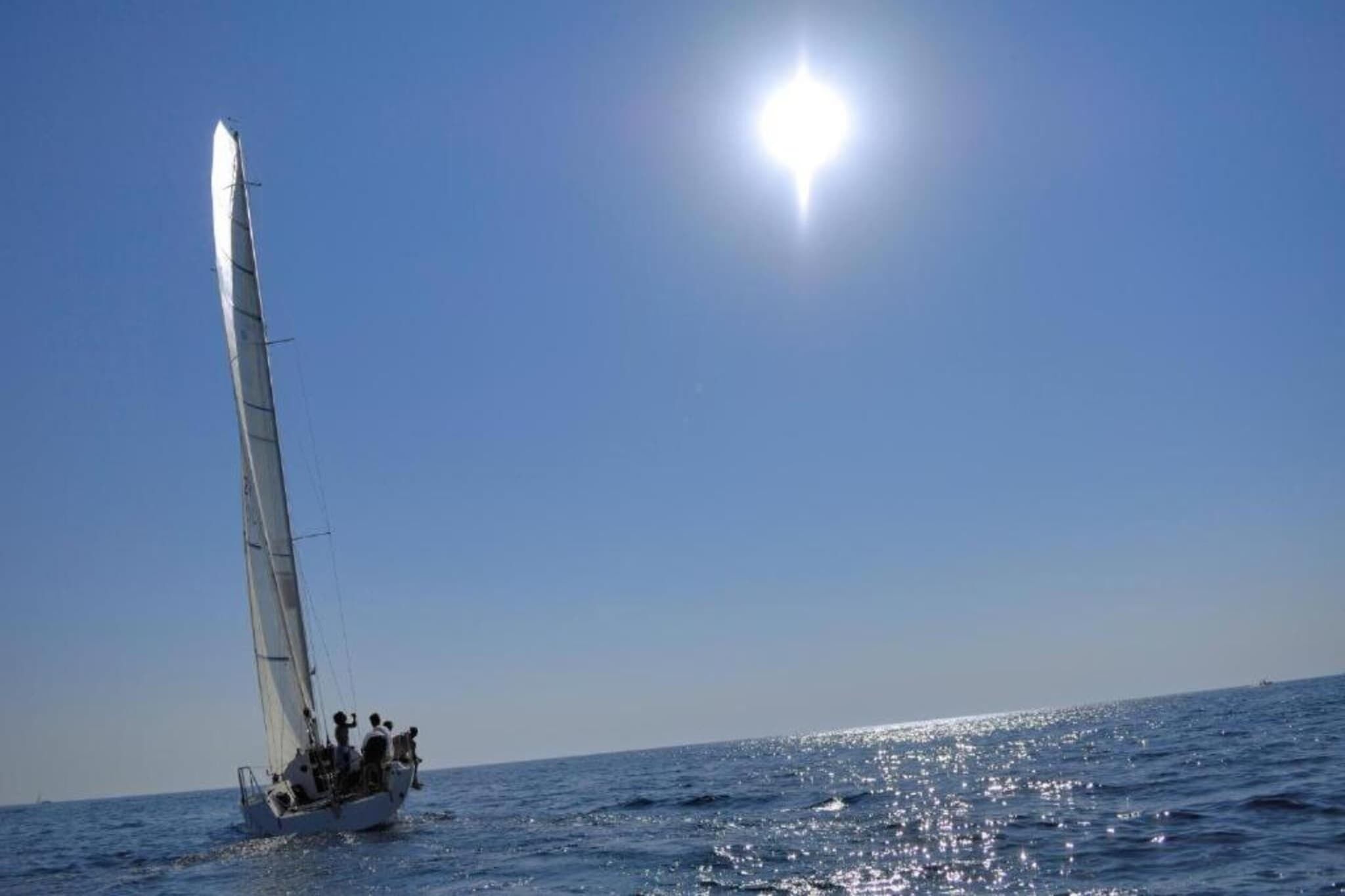 Un velero en el agua bajo un cielo despejado y con el sol brillando.