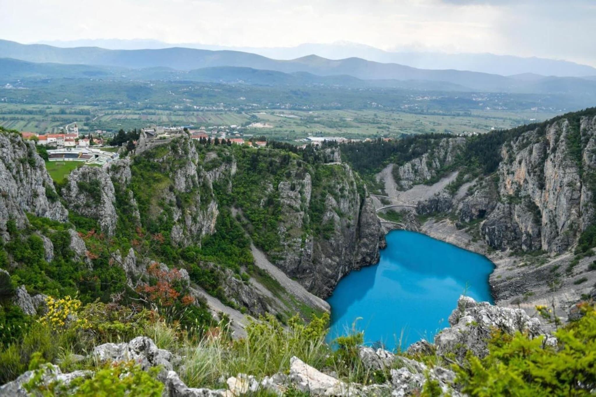 Un paysage montagneux avec un lac d’un bleu profond, entouré de falaises rocheuses et de verdure.