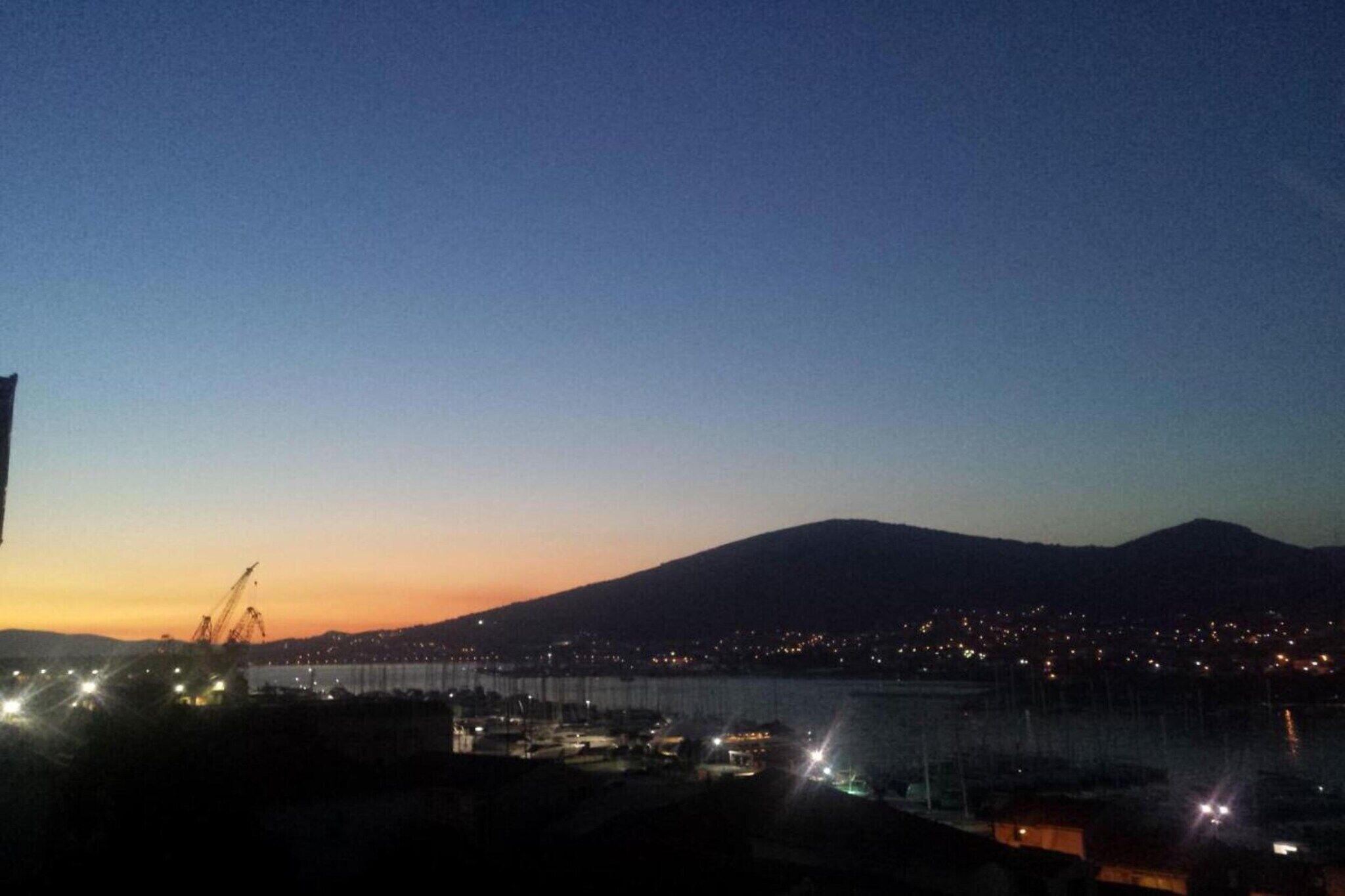 A nighttime view of a cityscape with a mountain in the background, a bridge, and construction cranes.