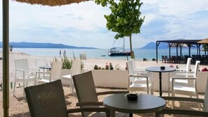 Un'area salotto in spiaggia con sedie e tavoli in vimini, con vista sul mare e una barca all'orizzonte.