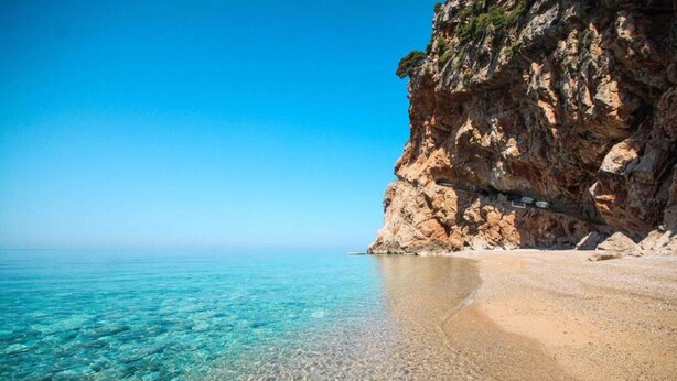 Una spiaggia limpida con una scogliera rocciosa e un cielo azzurro terso.