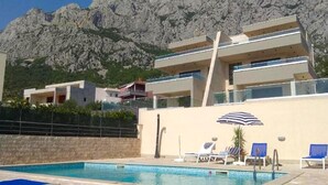 A modern building with a pool and lounge chairs, set against a mountainous backdrop.