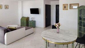 A living room with a sofa, a round table, a green cabinet, and a television mounted on the wall.