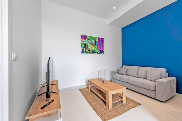 Un salon moderne avec un téléviseur à écran plat posé sur une table en bois, un canapé beige et un tableau abstrait aux couleurs vives accroché au mur.