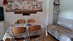 A dining area with a table set for four, surrounded by chairs, and a sofa in the background.