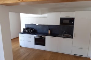 A modern kitchen with white cabinets, a black countertop, a built-in oven, a microwave, and a coffee maker.