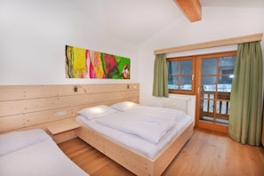 A room with a wooden bed, a window with curtains, and a colorful abstract painting on the wall.