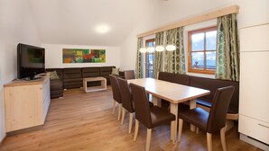 Ein modernes Wohnzimmer mit einem Holzesstisch, braunen Ledersesseln, einer Couch und einem Fernseher.