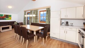 Ein Essbereich mit Holztisch und -stühlen, eine Küche mit weißen Schränken und ein Fenster mit Vorhängen.