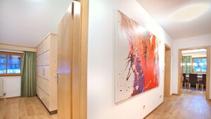 Ein Flur mit Holzboden, einem großen abstrakten Gemälde an der Wand und Blick in einen anderen Raum durch eine offene Tür.