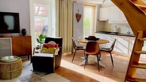 A modern living room with a sofa, a small round table, and a TV. There is a staircase leading to a kitchen area with white cabinets and a stove. - Nice holiday residence in De Koog near the beach (De Koog)