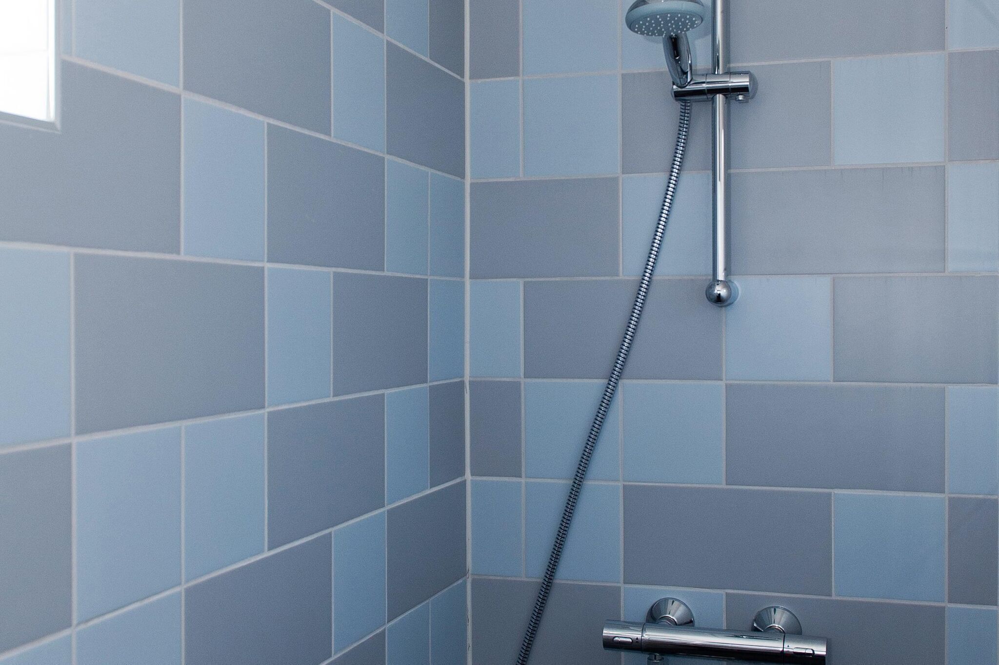 Eine Dusche mit Handbrause und am Wand montiertem Wasserhahn.