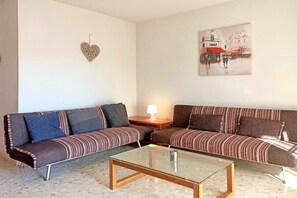 Una sala de estar con dos sofás, una mesa de centro de vidrio, una decoración con forma de corazón y un cuadro en la pared.