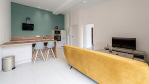 Ein modernes Wohnzimmer mit einem gelben Sofa, einer Küchenzeile mit einer Holzarbeitsplatte und einem Fernseher.