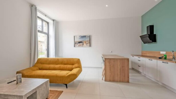 Ein modernes Wohnzimmer mit einer Couch, einem Couchtisch und einer Küchenzeile mit Schränken und einer Arbeitsplatte.