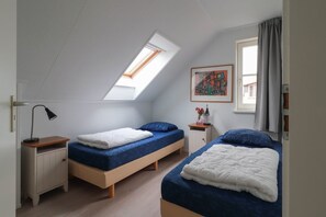 A dormitory room with two single beds, a skylight, a small cabinet, and a painting on the wall.
