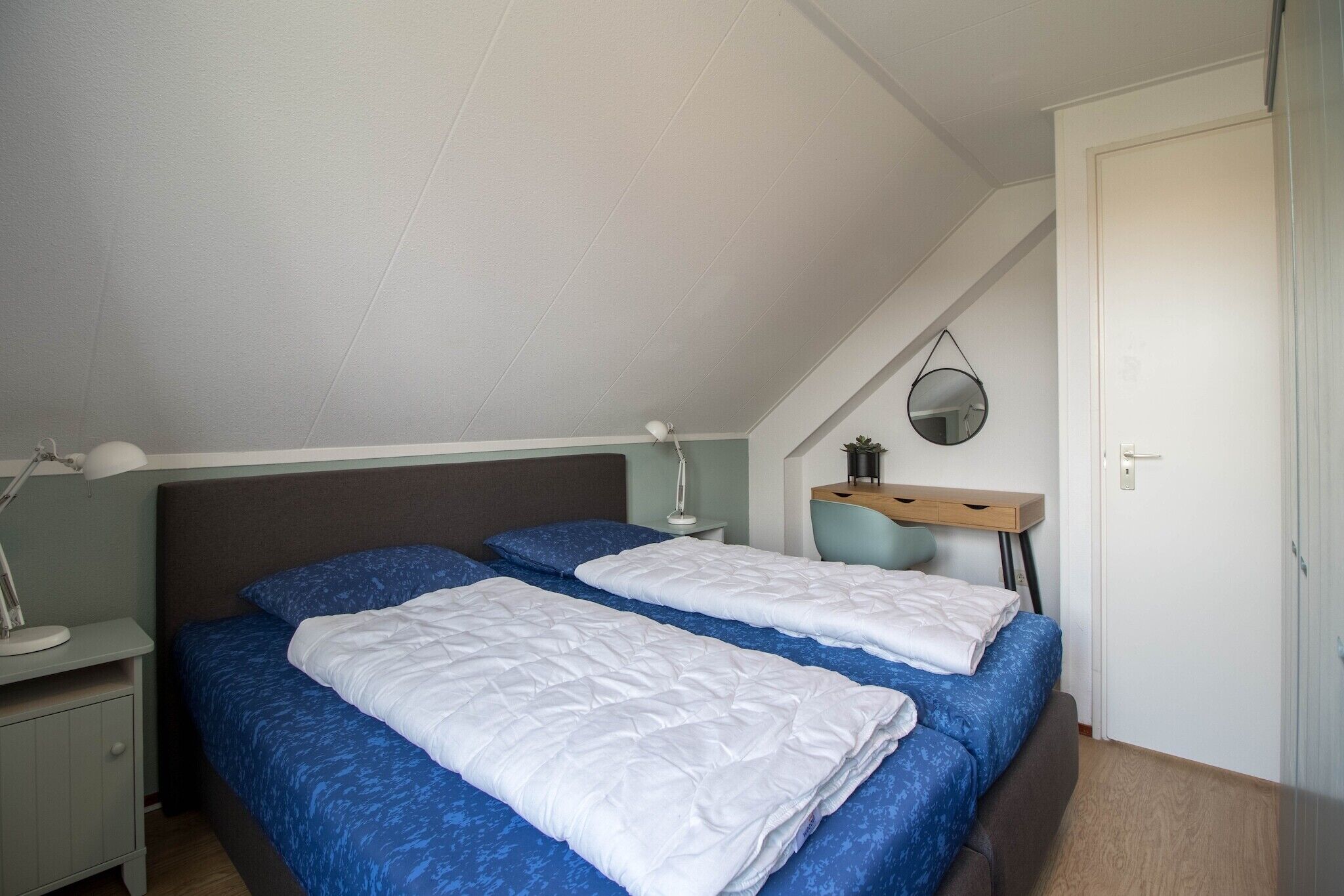 Ein Schlafzimmer mit zwei Betten, einem Schreibtisch, einem Stuhl, einem Spiegel und einer Tür.