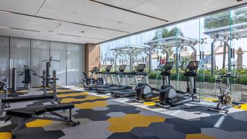 A modern gym with various exercise equipment, large windows, and a patterned floor.