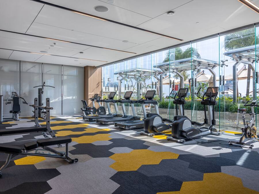 A modern gym with various exercise equipment, large windows, and a patterned floor.