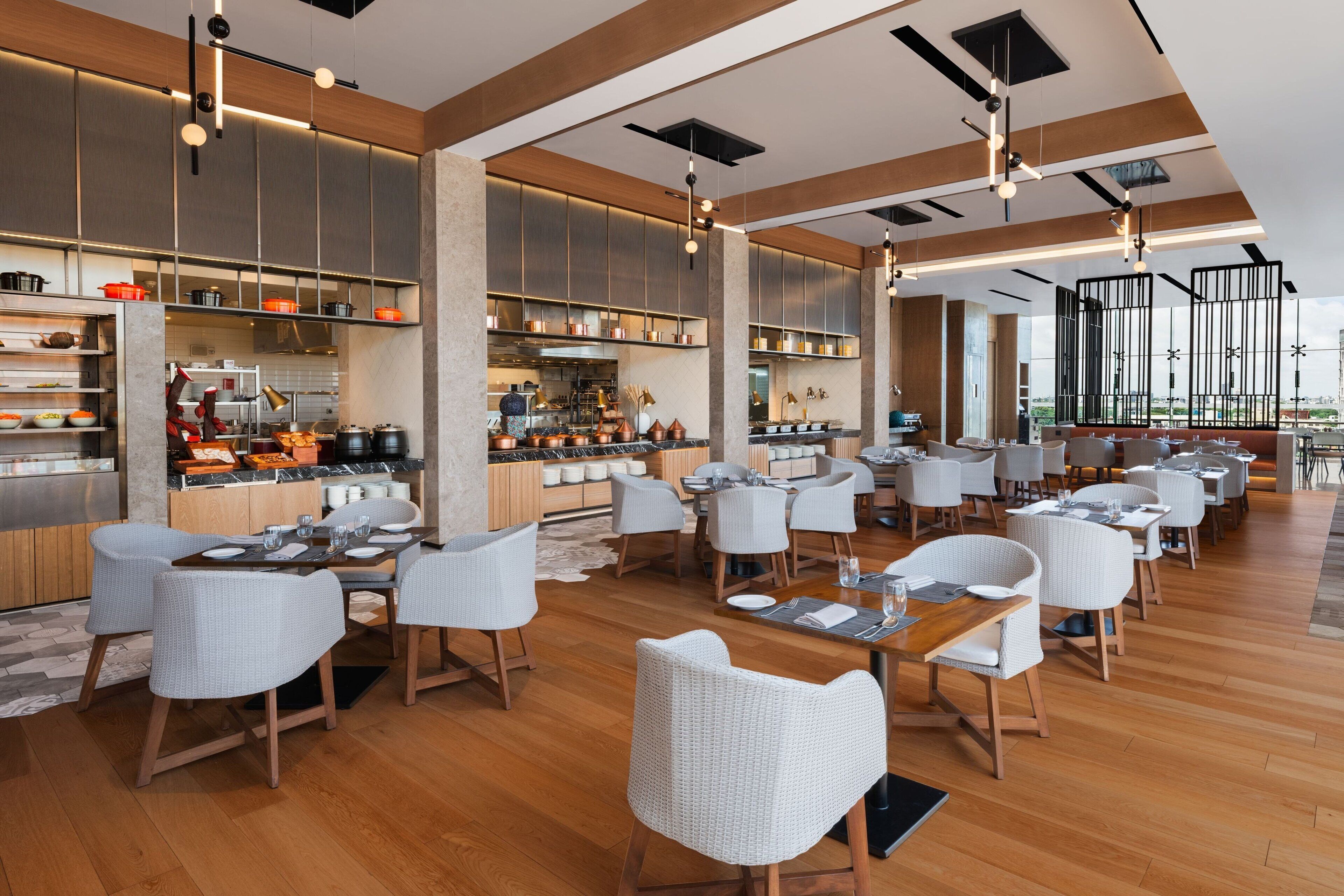 Un restaurante moderno con un amplio comedor, techos altos y una cocina visible al fondo.