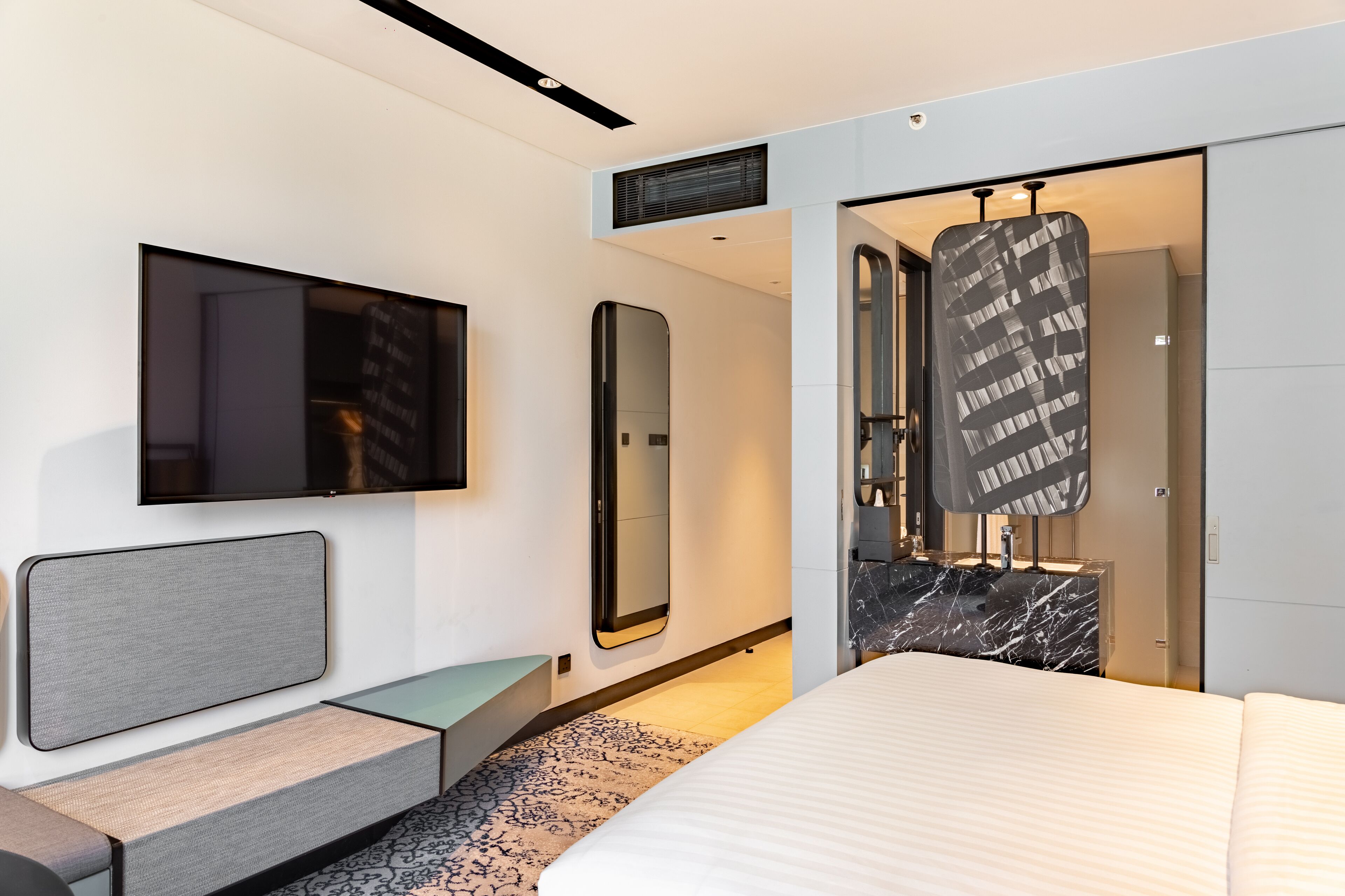 A modern hotel room with a large bed, a flat-screen TV, a mirror, and a wardrobe with a black and white patterned door.