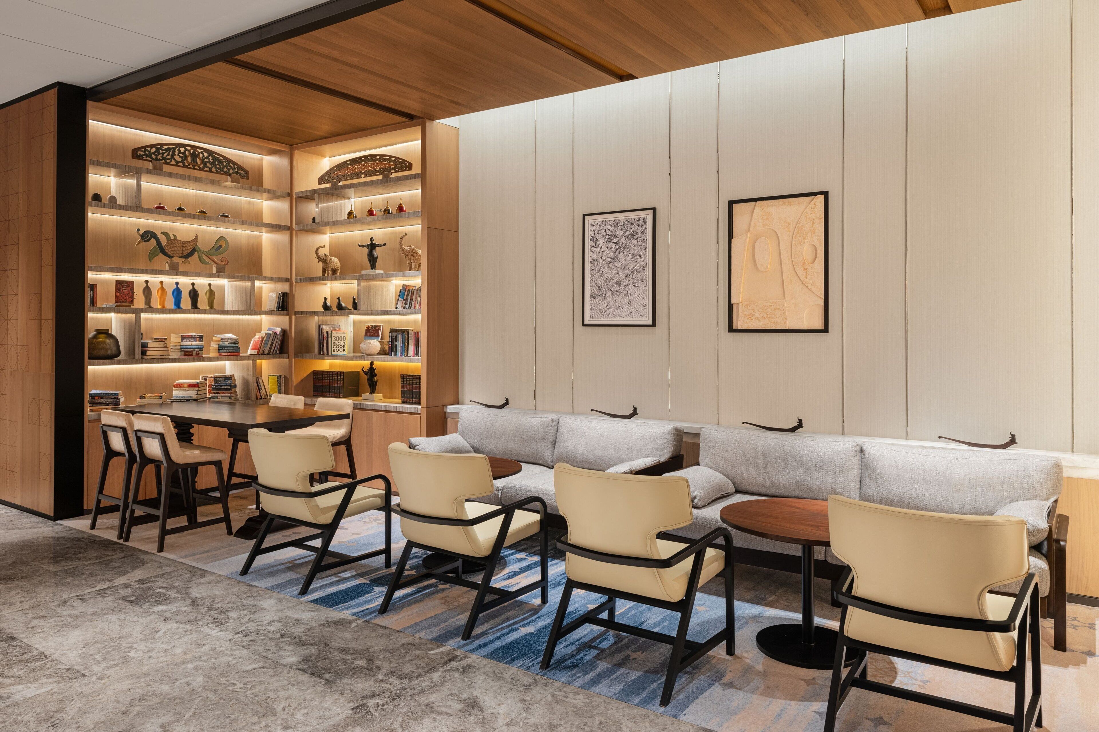 A modern hotel lobby with a seating area, a bookshelf, and a dining table.