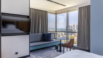 A modern hotel room with a large window, a sofa, a small table, and a bed.