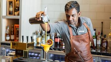 A bartender pouring a cocktail into a glass.