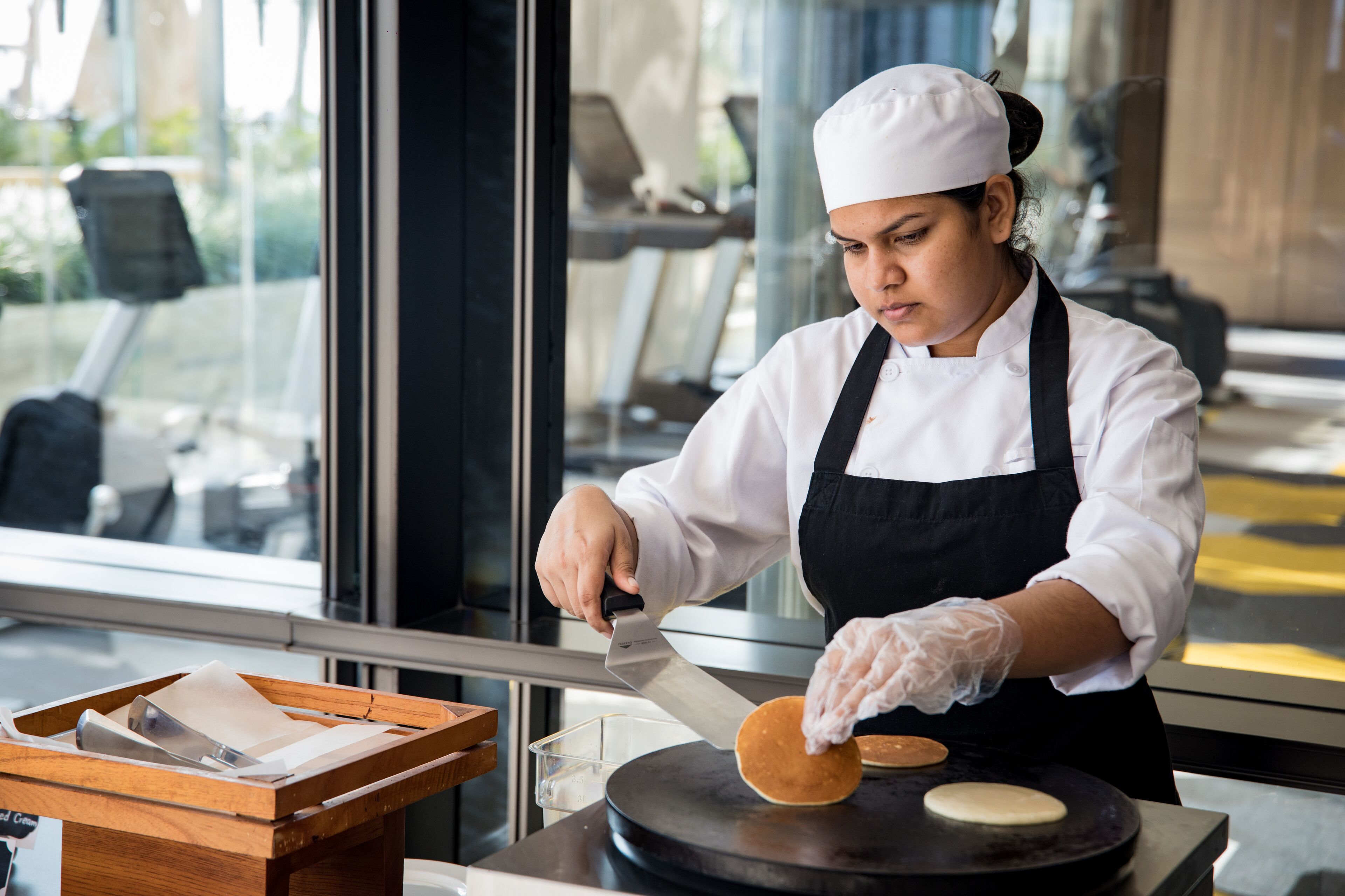 A person in a chef's uniform preparing food on a griddle.