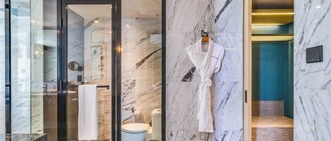 A modern bathroom with a glass shower enclosure, a white robe hanging on the wall, and a marble-tiled floor.