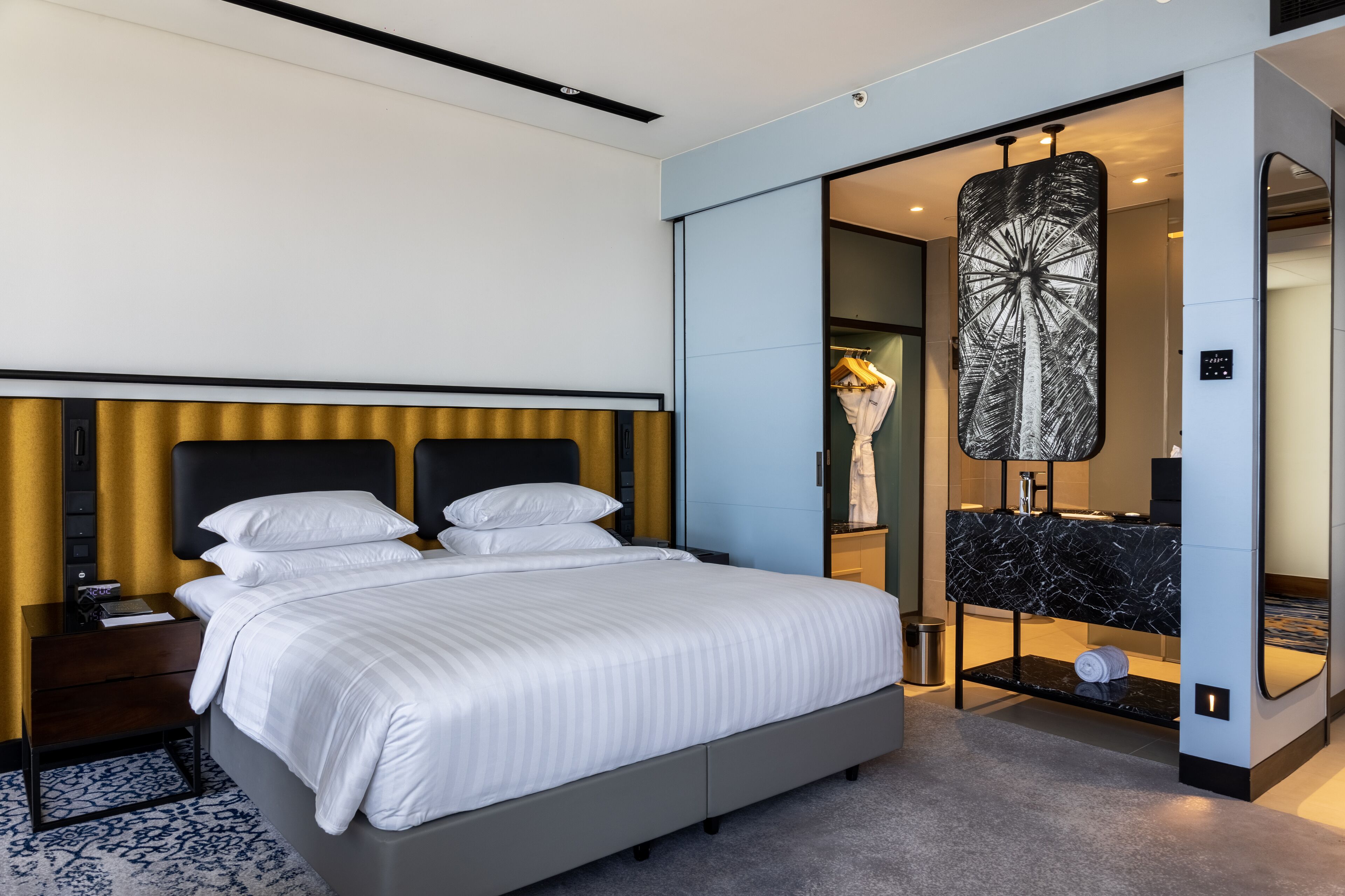 Een moderne hotelkamer met een groot bed, een inloopkast en een badkamer met een marmeren wastafel.