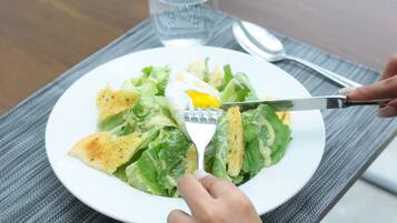 Un plato blanco con ensalada, un tenedor y una cuchara sobre una mesa.