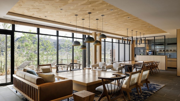 Un salón espacioso con una gran mesa de madera, asientos cómodos y vistas al exterior a través de amplios ventanales.