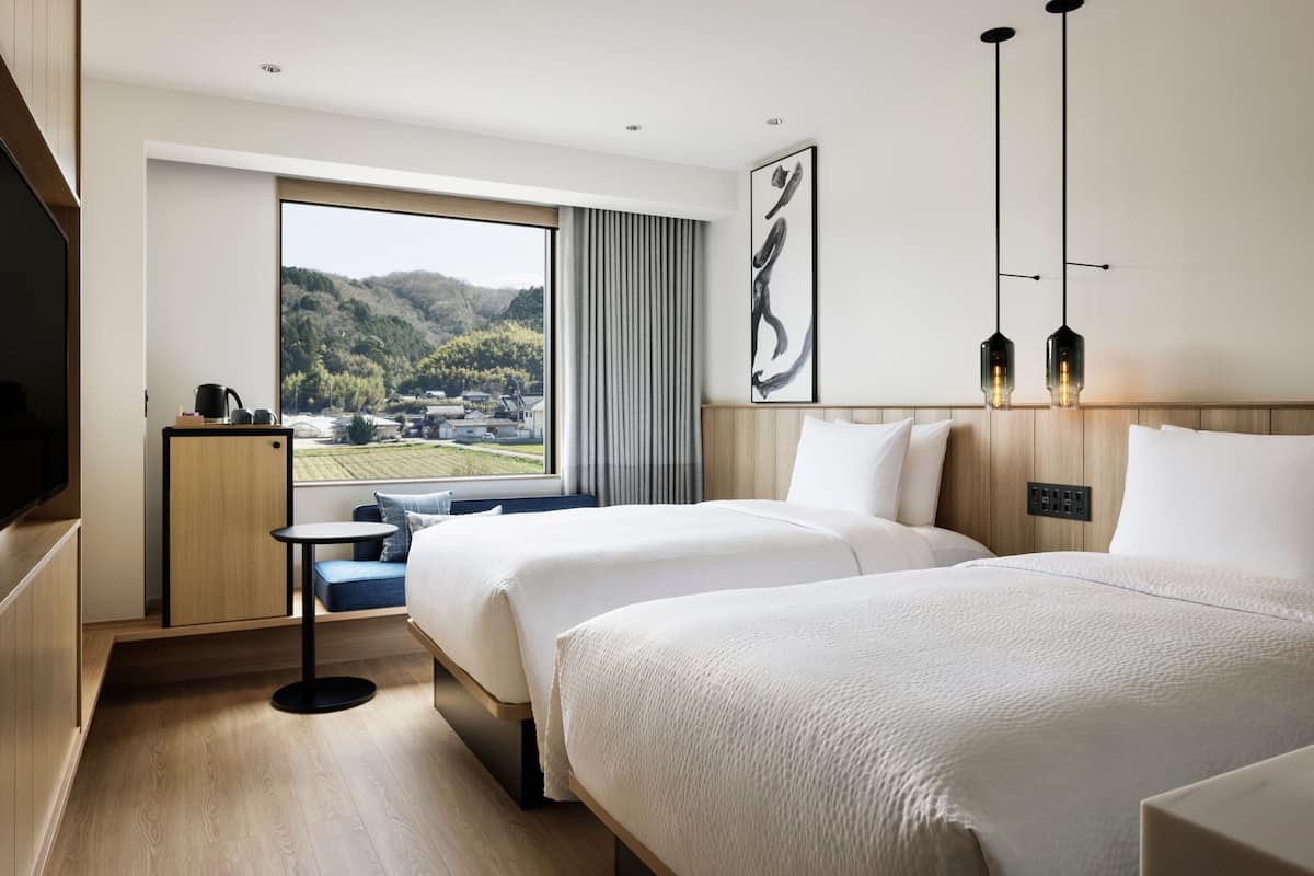Ein Hotelzimmer mit zwei Betten, einem Fernseher, einem kleinen Tisch und Blick auf eine gebirgige Landschaft.