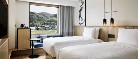 A hotel room with two beds, a TV, a small table, and a view of a mountainous landscape.