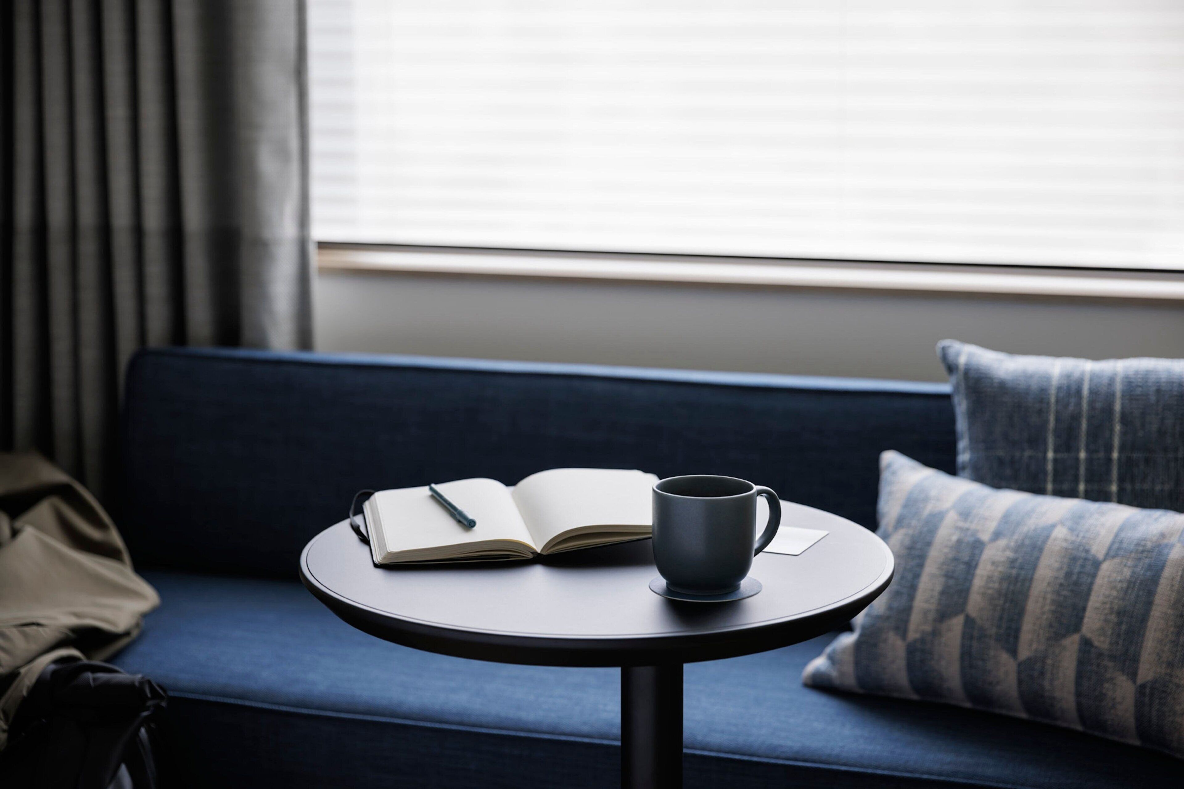 A round table with a book and a mug on a blue sofa.