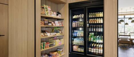 Una despensa bien organizada con estantes llenos de diversos alimentos y un refrigerador grande repleto de bebidas.