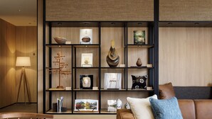 Una sala de estar moderna con piso de madera, un sofá de cuero marrón, una mesa de centro de madera y una estantería llena de objetos decorativos y libros.