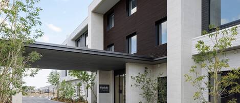 A modern building with a covered entrance, a sign reading "Fairfield," and a landscaped area with trees and shrubs.
